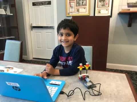 a boy sitting at a table with a laptop and toys