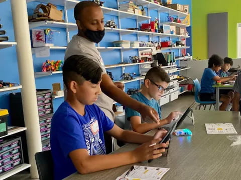 a group of boys sitting at a table looking at a tablet