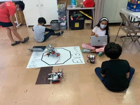 a group of children sitting on the floor with a laptop and a drawing