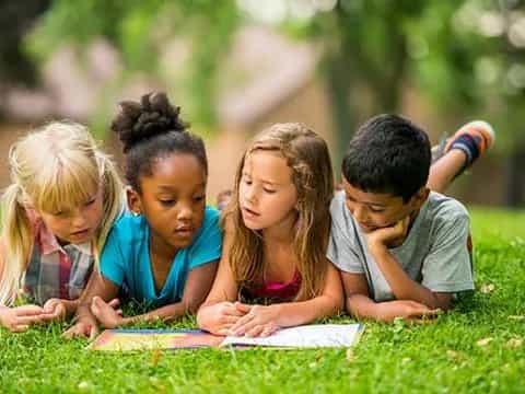 a group of children sitting on the grass writing on paper