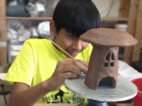 a young boy painting a clay pot