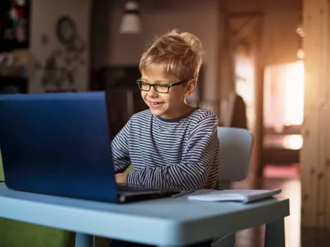 a boy sitting at a table with a laptop