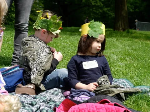a couple of girls sitting on the grass with a green hat on