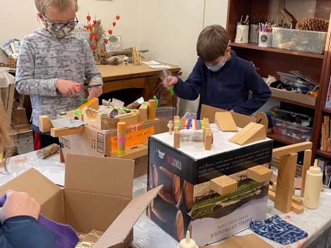 a couple of people in a room with boxes and a table with objects