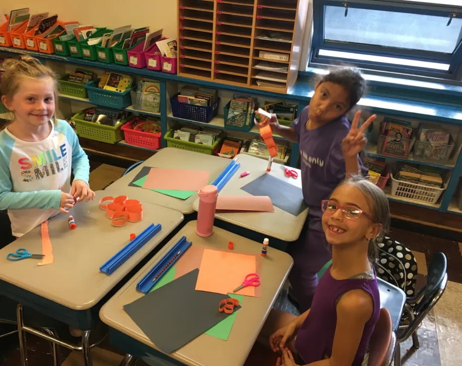 a group of children sitting at a table with colorful paper on it