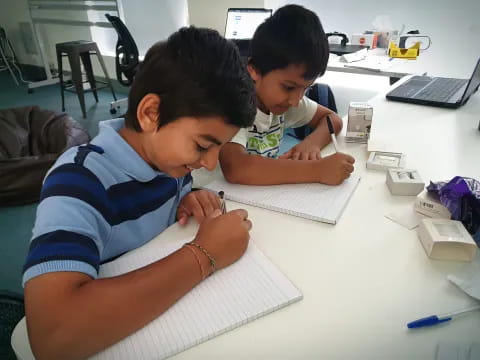 a couple of boys sitting at a table writing on paper