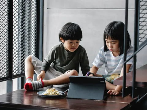 a couple of children sitting at a table looking at a laptop