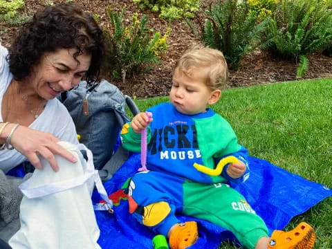 a person and a baby sitting on a blanket in a yard