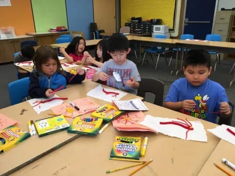 a group of children sitting at a table with books and pencils