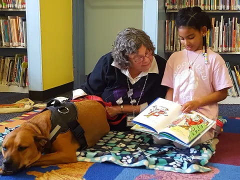 a person and a dog reading a book to a girl
