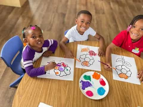 a group of children sitting at a table with art