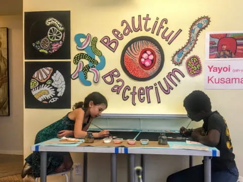 a woman and a man sitting at a table with a wall with art