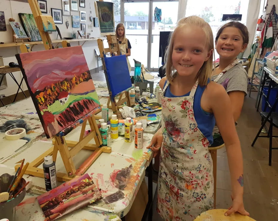 a couple of girls posing for a picture next to a table with art