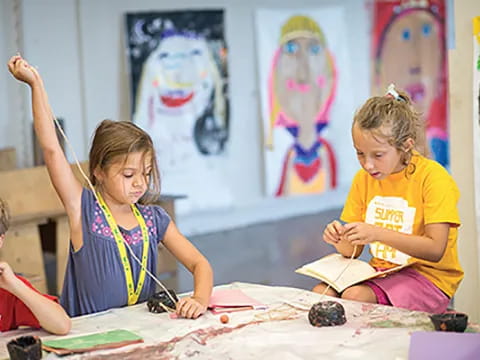 a group of children sitting at a table painting