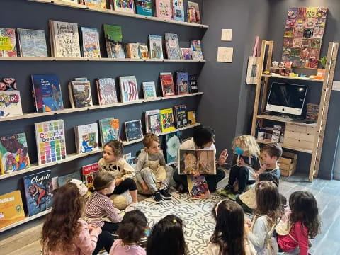 a group of children sitting in a room with shelves with books