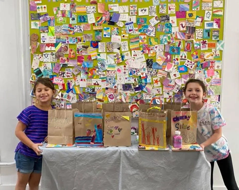 a couple of girls standing next to a table with a wall of art