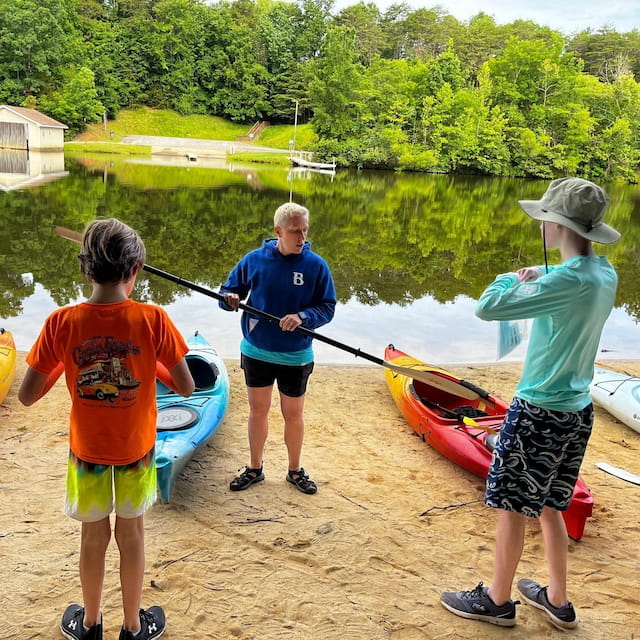 a group of people standing by a lake with a paddle