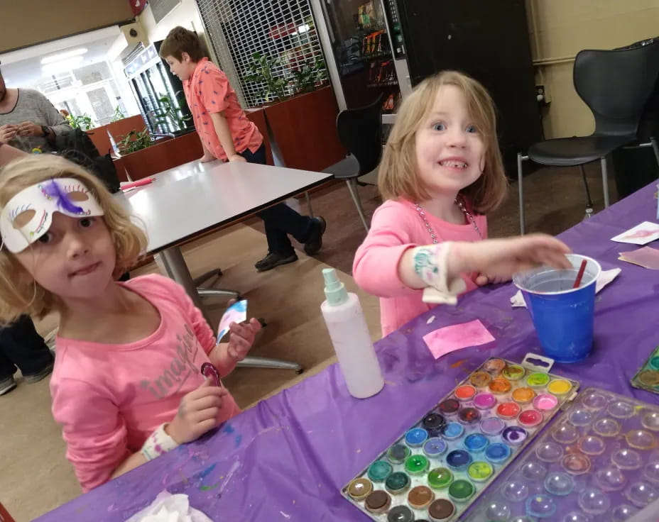 a couple of girls sitting at a table with colorful paper and a bottle