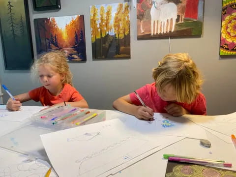 a couple of children sitting at a table with art on the wall