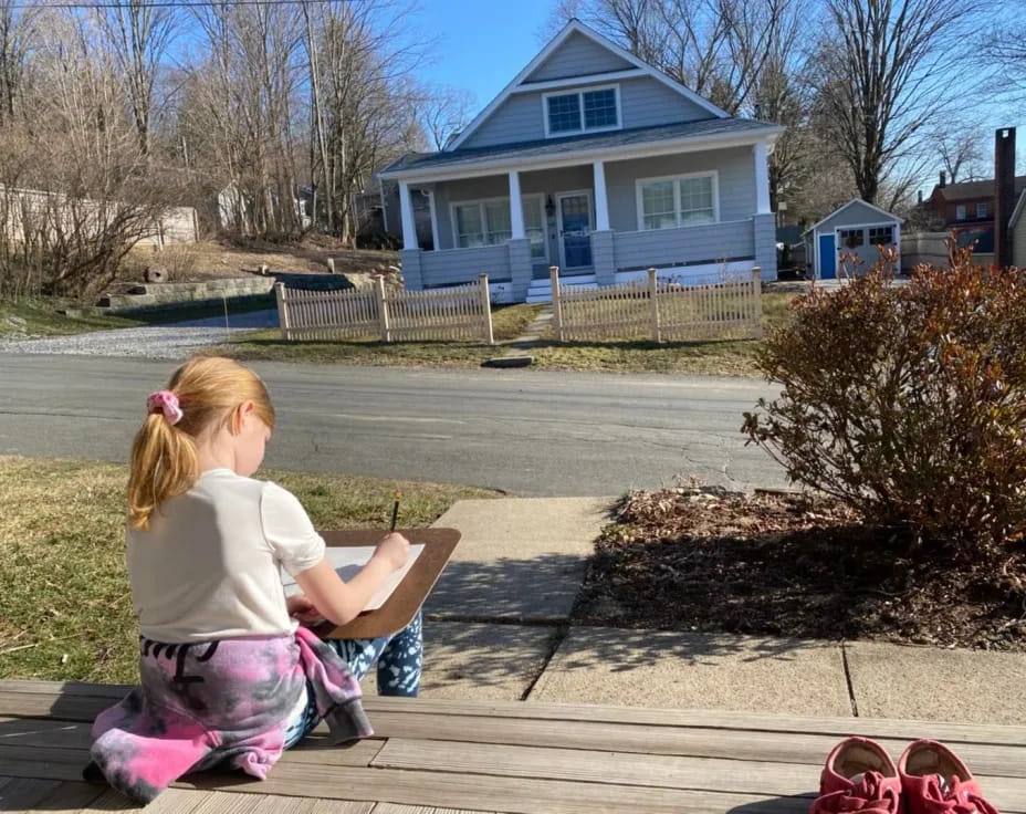 a girl sitting on a bench in front of a house