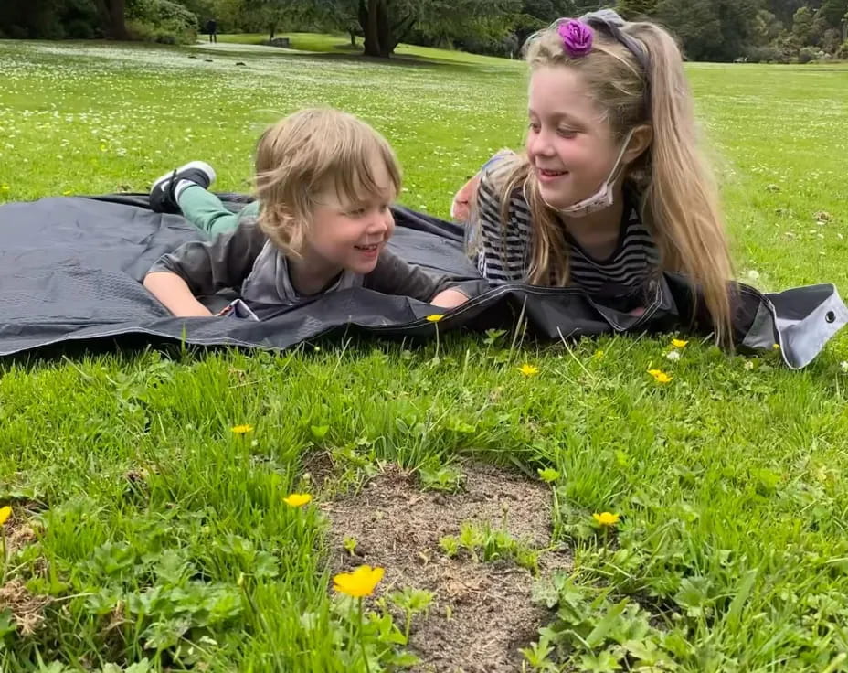 a couple of girls lying in a grassy field with flowers and trees