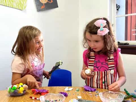 a couple of girls sitting at a table with food and toys