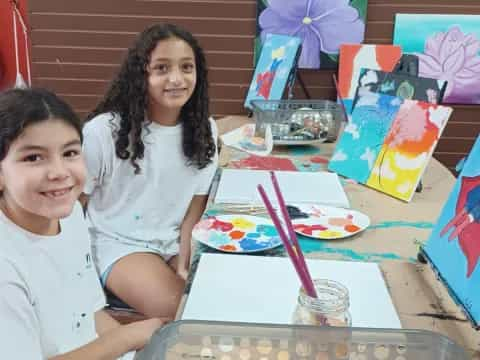 a couple of girls sitting at a table with colorful paper crafts