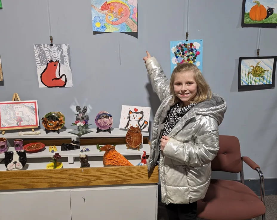 a girl standing in front of a desk with a chair and a shelf with toys on it
