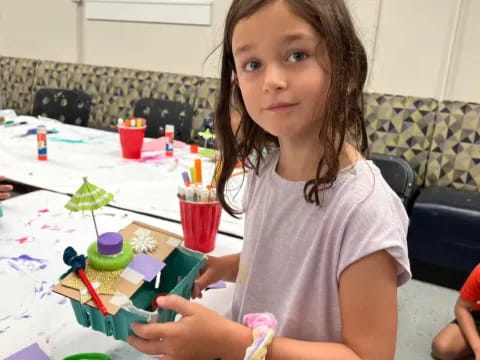 a girl sitting at a table with a toy