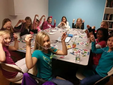 a group of children sitting around a table with their hands up