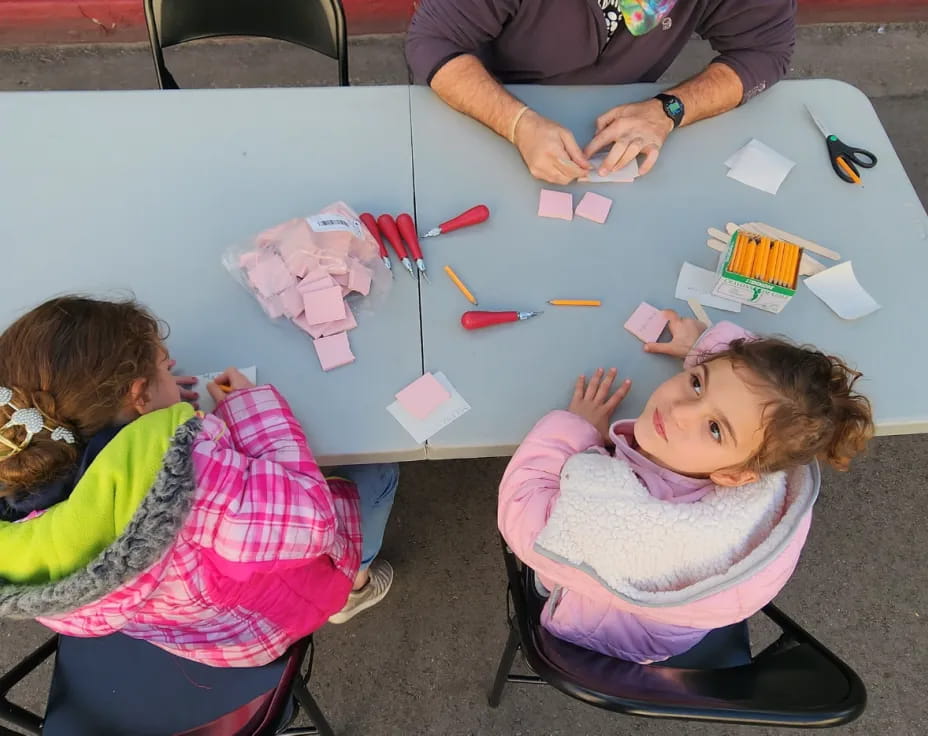 a group of children sitting at a table with colorful paper on it