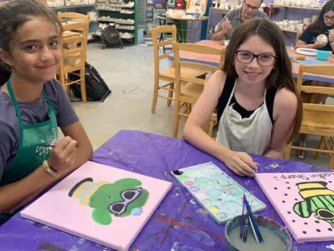 a couple of girls sitting at a table with art
