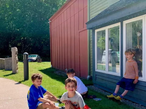 a group of kids sitting on the grass outside a house