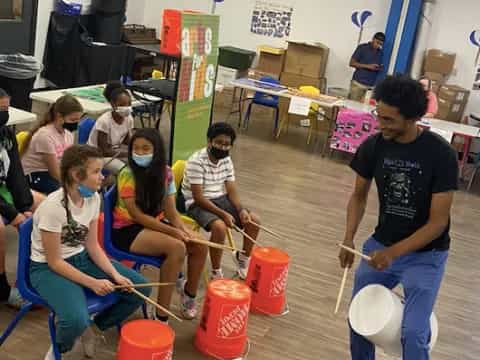 a group of people sitting in a room with buckets and a person holding a frisbee