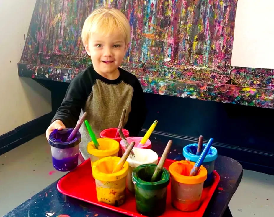 a child sitting at a table with colorful cups and a blue tablecloth