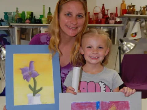a woman and a girl holding up paintings