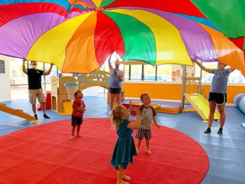 a group of children in a play area with a large colorful umbrella