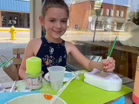 a girl sitting at a table with a child in the background