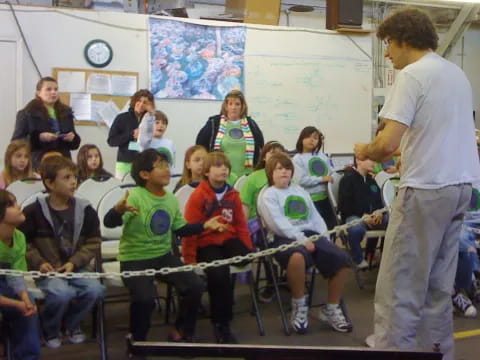 a person standing in front of a group of kids sitting on a bench