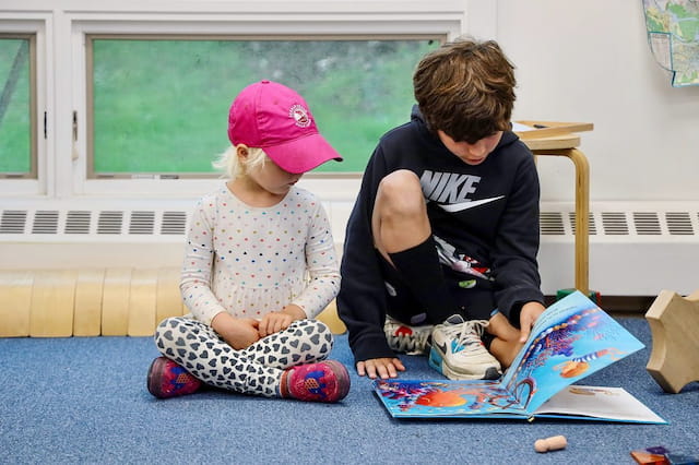 a boy and a girl sitting on the floor looking at a book