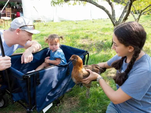 a man and woman holding a baby and a chicken in a stroller