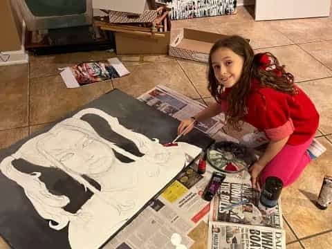 a girl sitting on the floor with a pile of magazines and a bottle of soda