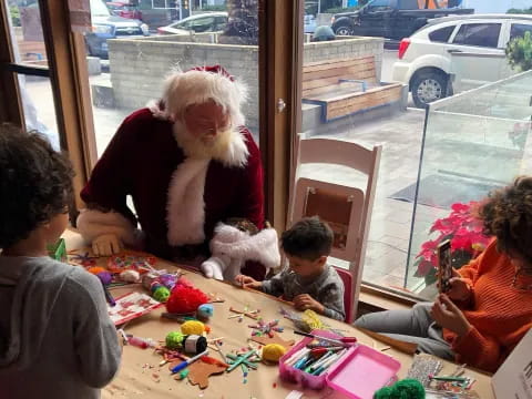 a person and children sitting at a table with a santa claus