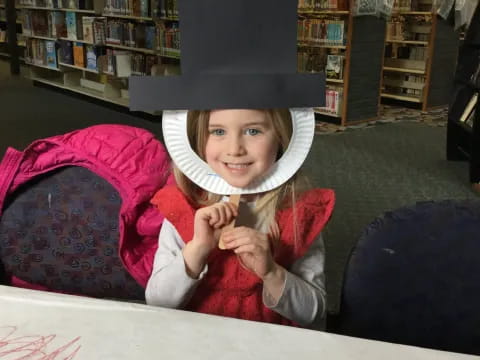 a girl wearing a hat and sitting at a table in a library