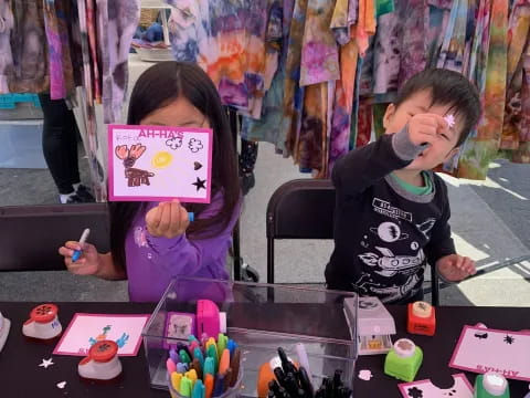 a boy and girl sitting at a table with a book and toys