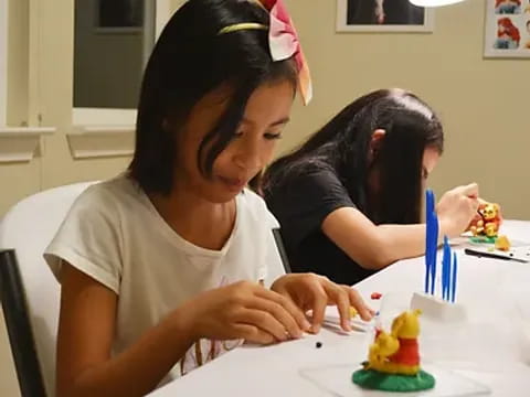 a couple of girls sit at a table with a birthday cake