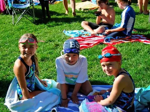 a group of children sitting on a blanket on the grass