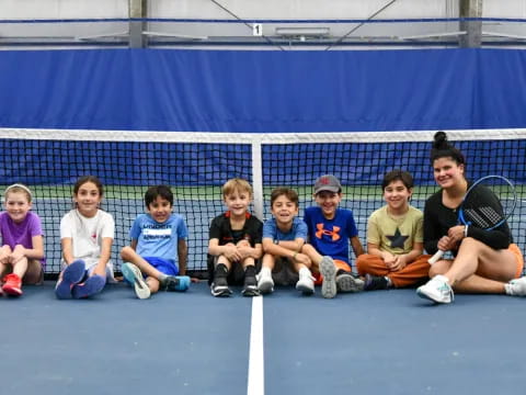 a group of kids sitting on the ground with a tennis racket