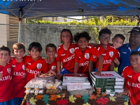 a group of people wearing matching red shirts standing next to a table with food on it