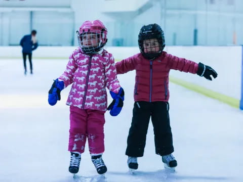 a couple of kids wearing helmets and ice skates on ice
